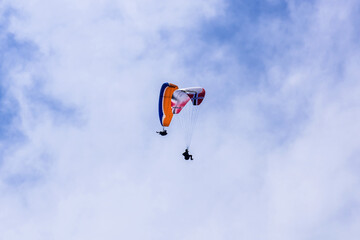 Paraglider flying against the blue sky with colorful wing above the clouds.