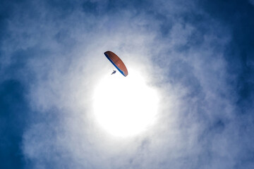 Paraglider flying against the blue sky with colorful wing above the clouds.