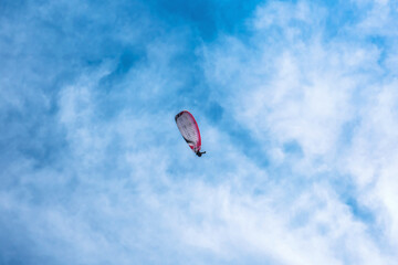 Paraglider flying against the blue sky with colorful wing above the clouds.