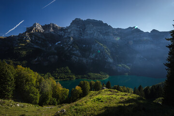 Late afternoon view over Swiss mountain lake. Meadow and tree line in the foreground, mountain face in the background.