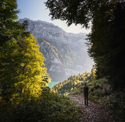 Woman hiking through forest in the swiss alps. Colorful sunset atmosphere.
