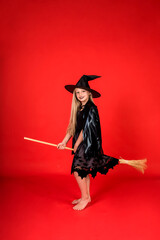 girl in a witch costume sits on a broom on a red isolated background with a copy of space