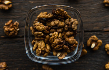 Walnut in a smale plate with scattered shelled nuts and whole nut which standing on a wooden vintage table. Walnuts is a healthy vegetarian protein nutritious food. Walnut on rustic old wood.