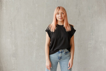 Young girl wearing blank black t-shirt. Concrete wall background. Horizontal