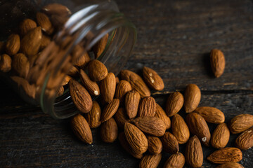 Almonds scattered on the wooden vintage table from a jar. Almond is a healthy vegetarian protein nutritious food. Almonds on rustic old wood.