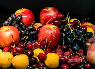 Mix of fresh berries and fruits on dark background. Peaches, apples, apricots, dark blue grapes, red cherries, blueberry , raspberries