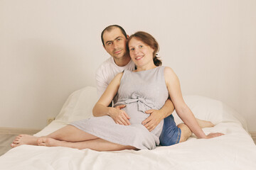 Smiling man embracing happy pregnant woman sitting on couch holding tummy with .