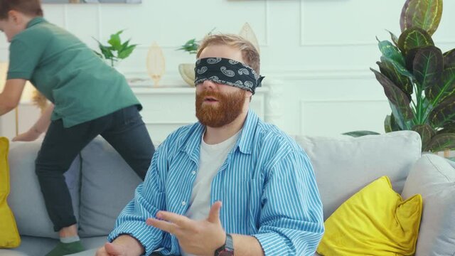 Family playing hide-and-seek indoors. Blindfolded bearded father counting while his tricky son searching hide places in the apartment. Funny activity.