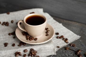 Coffee cup with scattered coffee beans on a wooden table background. Mug of black coffee on a linen textile.