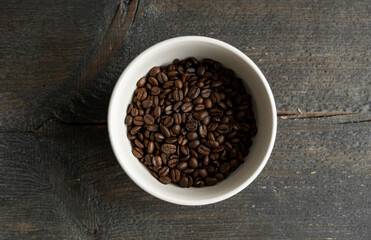 Bowl filled of fresh arabica or robusta coffee beans on a wooden table.