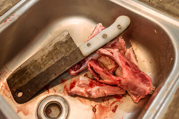 A meat cleaver and pig jawbones inside a stainless sink of a kitchen or market.