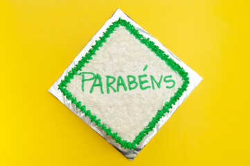 Birthday cake decorated with green icing and grated coconut. Isolated on yellow background. Top view. Translation of the word PARABÉNS in English: CONGRATULATIONS.