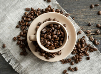 Coffee cup filled of fresh arabica or robusta coffee beans with scattered coffee beans on a linen textile and wood table.