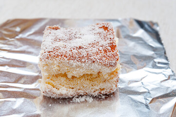 Traditional Brazilian dessert (known as Bolo Gelado) - Making step by step: Cake piece with grated coconut in aluminum foil. Close-up.