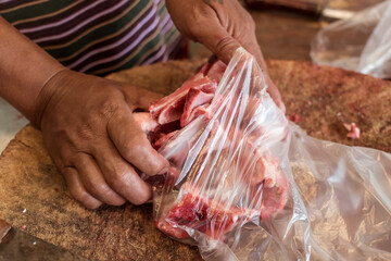 Placing chopped pork chunks into a clear plastic bag at a local market.