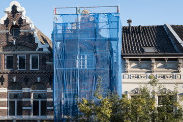 Fototapeta premium Scaffolding with protective net against historic building to prevent paint and building material from falling on the street and people, during renovation in a street in Maastricht, the Netherlands