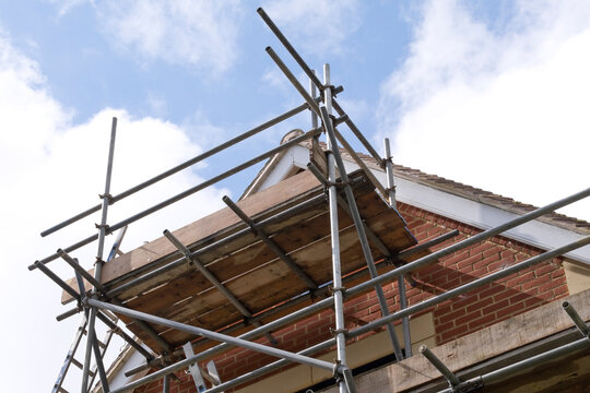Modern house roof construction with scaffold pole platform. New build domestic building against blue sky with clouds