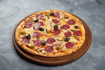 Baked Italian pizza with salami, olives, mushrooms on a wooden tray on a gray background. Caesar pizza
