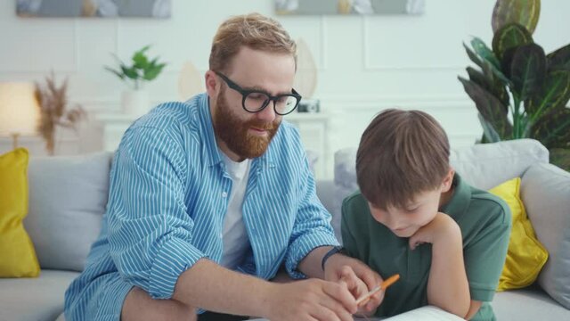 Euphoric son and daddy playing video games on controller. Tricky young family pretending doing fake homework exercises when mom comes home. Fun, humor concept.