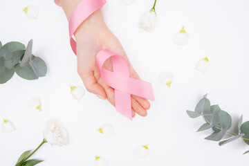 Obraz na płótnie Canvas Girl hands holding pink breast cancer awareness ribbon on white background with flowers. Concept healthcare and medicine beauty care skin. Top view