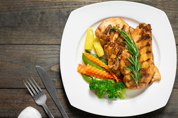 Steak chicken with rosemary and vegetables in white plate on wooden table.
