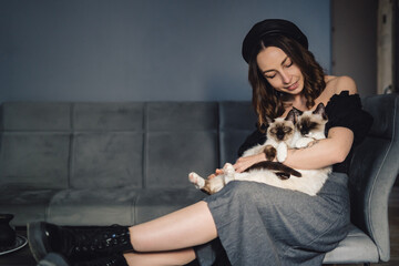 Attractive girl embracing her Siamese cats. Indoor portrait of cute woman playing with her two pets.