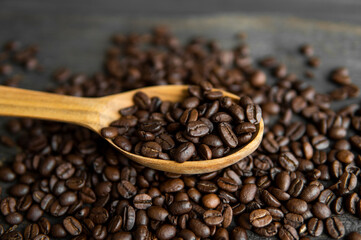 Fresh roasted arabica coffee beans in a wooden spoon and scattered coffee beans on a wooden table.