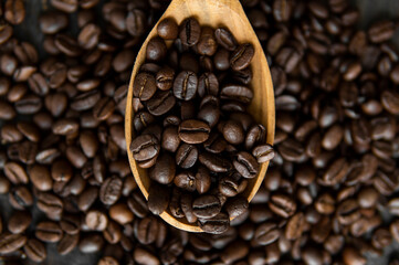 Fresh roasted arabica coffee beans in a wooden spoon and scattered coffee beans on a wooden table.