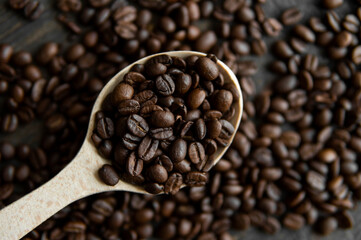 Fresh roasted arabica coffee beans in a wooden spoon and scattered coffee beans on a wooden table.