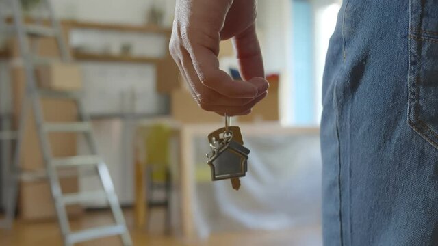 Close up of man holding key with house keychain in hand and walking in new apartment