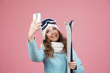 fun skier takes a selfie on her smartphone. A young woman with ski equipment in a jacket and hat,