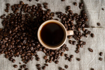Coffee cup with roasted coffee beans on linen background. Mug of black coffe with scattered coffee beans. Fresh coffee beans.