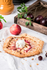 Homemade galette with peaches and ice cream on light background
