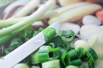 Green onions with a knife on the kitchen table close up with side light