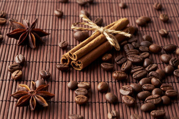 Roasted whole coffee beans, tied sticks of cinnamon and anise on a dark background