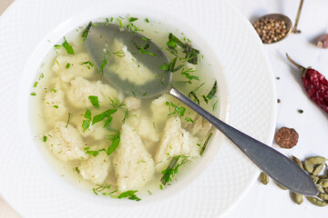 Chiken broth with dough and herbs in plate on white wooden background with spoon and spices