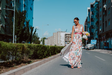 Young beautiful stylish caucasian woman model in summer dress with flower box in her hand on the street
