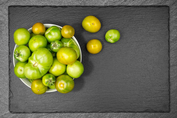 Green tomatoes in an enamel sieve on slate slab with copy space