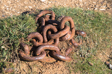 Obraz premium Rusty chain coiled on the ground in the grass