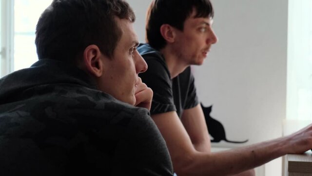 Two young men looking in the same direction and communicate sitting at home