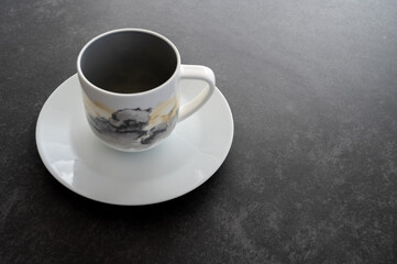 A coffee cup placed on a white saucer placed on a dark stone table with copy space