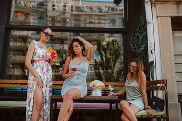 Three beautiful young caucasian women in short summer dresses are sitting and drinking cocktails in the cafe garden. Girls at parties