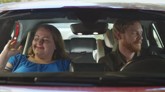 View through windscreen of happy young parents getting out of car going for children
