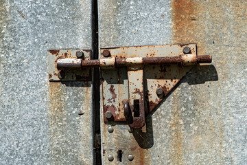 Old rusted grungy metal garage door with latch and hasp. Close up of rusty vintage lock on closed door