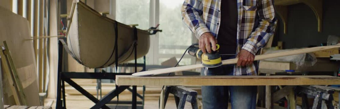 Mid 50s Caucasian male sanding a hand made canoe paddle in his workshop. Boat making hobby, small business owner