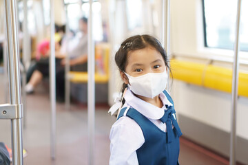 Asian child student or kid girl smile wear face mask in sky train or electric train with...