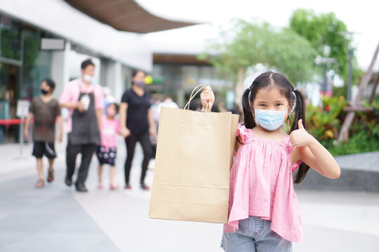 Asian Child Or Kid Girl Smile Wear Face Mask And Holding Empty Recycle Paper Bag To Enjoy Shopping And Fun With Thumb Up For Like And Good At Department Store Or Market Mall To Family Holiday On Covid