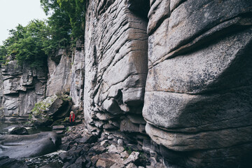 Woman in red coat standing next to stone wall of the cliff in Ukrainian Buky Canyon
