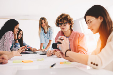 Group of male and female intelligent students making photo of graphic sketch and using internet connection on laptop while studying course of design with teacher sitting in university interior