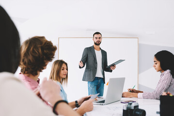 Successful male speaker talking with international students about business management during productive training in stylish college interior,portrait of talented coach during workshop indoors